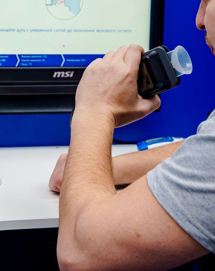 A man uses a breathalyzer device in a medical facility during the day.